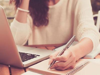 Female student looking at laptop and taking notes on paper.